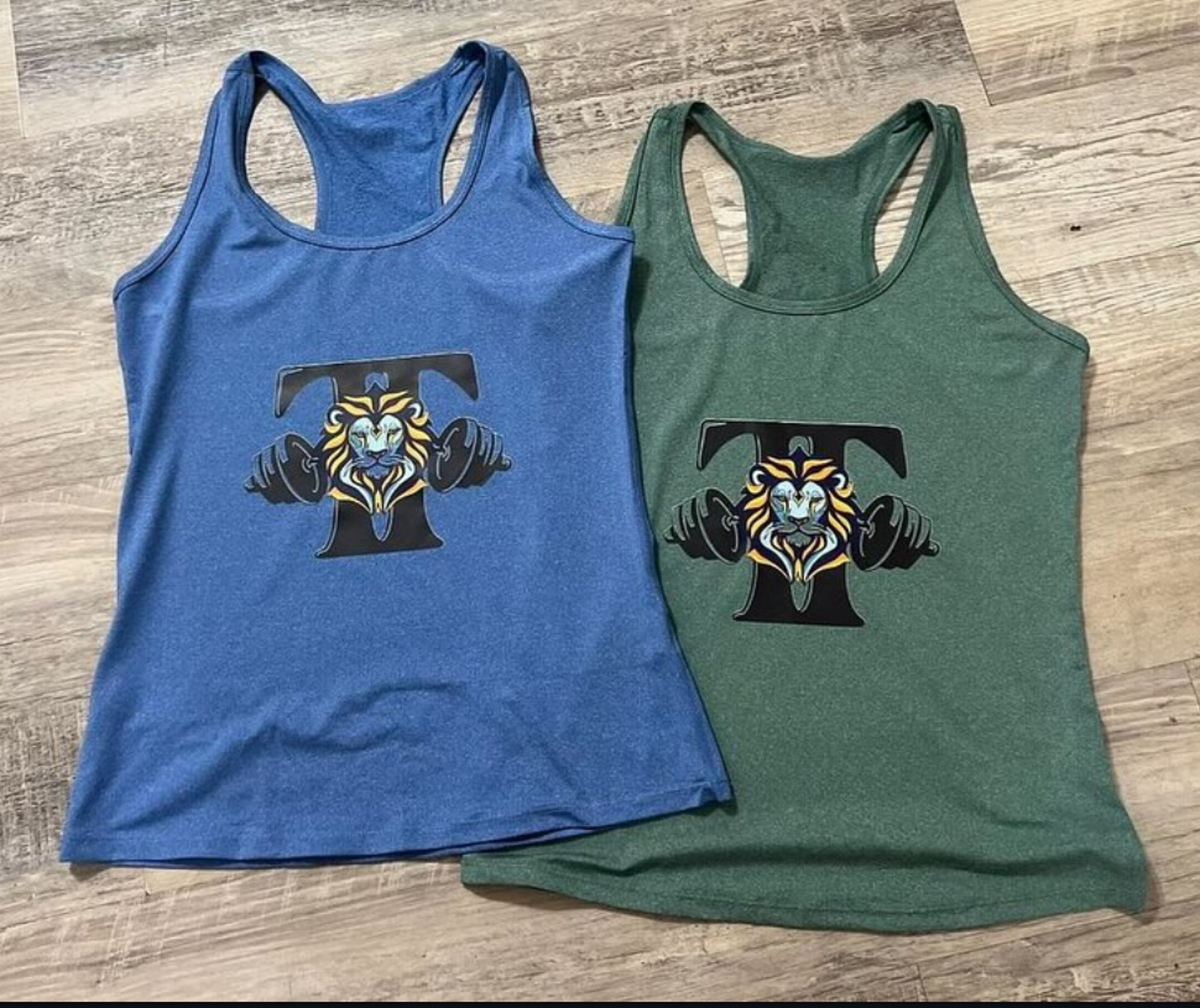 Women’s racerback tank tops in heather blue and forest green with Toussaint Training lion T logo.